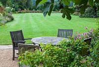 Wooden table and chairs on gravel area, with view over main lawn and topiary 'Forest' beyond. 
