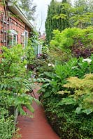View down the brick-paved path next to the studio extension, with borders of lush planting.