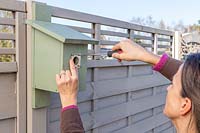 Woman attaching metal guard to bird box entrance with screw driver. 