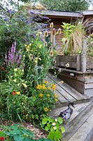 The eco house and deck surrounded by flowering plants. 