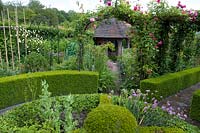 An ornamental kitchen garden with roses climbing over arches, clipped Buxus - box edging and a herb wheel edged with Hedera - ivy