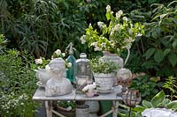 Old decorative objects displayed on vintage table, mostly white items set against greenery in a garden
