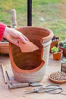 Woman adding crock to bottom of pot to prevent compost draining with water. 