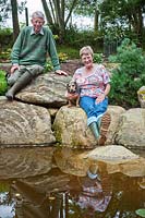 Margaret and Iain Gimblett with pet dog sitting on boulders by the edge of the pond. 