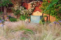 Clematis 'Sweet Sentation' grows in swags across the wall next to the terrace. In the foreground, mass planting of Stipa tenuissima Is punctuated with clipped Buxus sempervierens spheres. 

