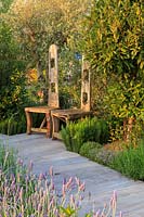 The Retreat, show garden featuring tall, rustic, sculptured wooden seats 
on a lime-washed decking pathway, with mature olive trees - Olea europaea,
 Lavender - Lavandula, Rosemary - Rosmarinus, Thyme - Thymus and Bay - 
Laurus nobilis.