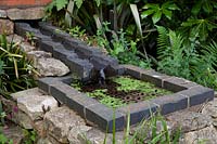 Raised brick rill feeding water into a well with metal grill
