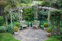 View of circular seating area and pergola in private garden. 