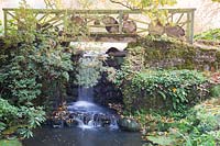 Decorative wooden bridge over waterfall in autumn garden. Minterne Gardens, Dorset, UK.
