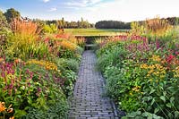 Double herbaceous borders with a paved path leading through to the bench. 
