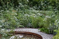 Circular pool edged with a cobbled path and herbs. The Health and Wellbeing Garden, designed by Alexandra Noble, sponsored by CED Ltd, Majestic Trees, Marshal Murray, Hampton Court Palace Flower Show, 2018

