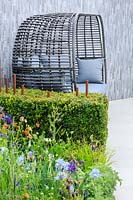 A grey basket-weave seat with grey cushions sits against a wall clad with light and dark grey split-faced porcelain. The Habit of Living â€“ A Garden In Support of Diabetes UK, designed by Karen Tatlow and Katherine Hathaway. RHS Malvern Spring Festival, 2019. 