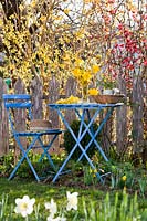 Blue table and chairs decorated with yellow floral arrangements in garden.