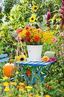 Bucket of summer flowers including Zinnias, Rudbeckia, Solidago, Monarda, Dahlia and Helianthus - Sunflowers, on table in wild garden.

