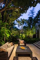 Modern seating area surrounded by lush tropical planting at night. Florida, USA. Garden design by Craig Reynolds Landscape Architecture.