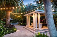 Paved shelter with pillars with furniture and string lighting. The Jones Residence, Key West, Florida, USA. Garden design by Craig Reynolds.