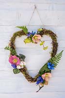 Mossed Heart-shaped wreath decorated with Helleborus, Muscari, ferns and Cyclamen leaves.
