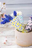 Tiny spring posies of Muscari and Narcissus blooms wrapped in origami blossom papers displayed in pottery vase. 