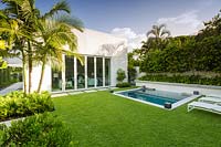 View across Zoysia grass lawn to back of house with sliding doors and small swimming pool and raised bed of Citrus - Orange trees