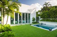 View aross Zoysia grass lawn to back of house with folding doors by swimming pool and raised bed of Citrus - Orange trees