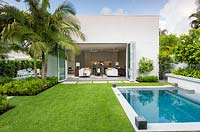 Layout of garden looking back at the house with its open folding doors, Zoysia grass lawn, swimming pool and small beds of foliage including Archontophoenix alexandrae - Palm
