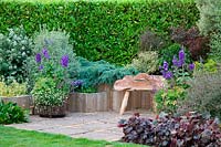 Seating area surrounded by raised beds planted with shrubs and perennials. Designer Karen Tatlow's garden, Lichfield