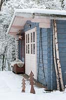 Blue, wooden cabin in snowy garden with Christmas decorations. 