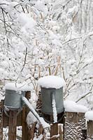 Two watering cans covered by snow on a fence.