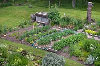 Overview of the vegetable garden surrounded by lawn. Features include: Strawberry  bed, row of Potato and climbing Pea plants up supports
and a compost heap and pin tree trunk with bird feeders