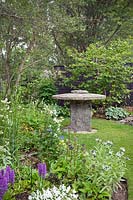 Old millstone used as a table with planted herbaceous borders 
including Hosta, Geranium, Dactylorhiza elata - Marsh Orchid-, Centaurea, 
white Viola and Thalictrum