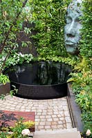 'The Thrive Reflective Mind' garden with raised pond set on paving with sculpture within hedge
