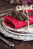 Place setting with wicker mats plus red linen napkin, cones and candle tied up with string