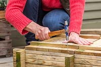 Woman fixing bottom plate to planter using hammer and nails