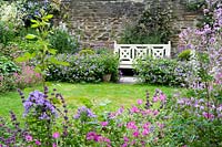 White painted bench set between full flowering borders at Bosvigo House, Cornwall, UK.