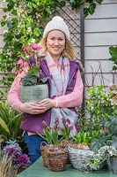 Woman holding pot of pink hellebore in early-spring courtyard setting.