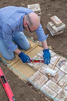 Man using short spirit-level to check that newly laid bricks are level. 