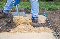 Man adding gravel to form base of path using a shovel. 