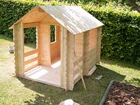 A child's wooden playhouse in front of a Carpinus betulus hedge. 