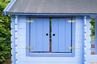 Window of a Blue painted children's playhouse in garden. 