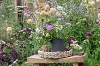 Cut flowers in a jug in front of an overgrown flower border in the BBC Springwatch garden at RHS Hampton Court Flower Show 2019 - Designed by Jo Thompson in consultation with wildlife gardener Kate Bradbury