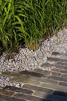 Brick pathway edged with coarse stones in show garden. The South West Water Green Garden, designed by Tom Simpson, Sponsored by South West Water, RHS Hampton Court Flower Show, 2018.
