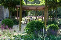 Wooden pergola and shaded dining area in modern garden, with clipped Box balls. 