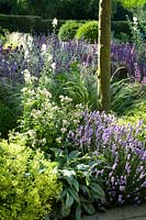 Borders of ornamental grasses and flowering perennials create soft texture, planted under trees.
