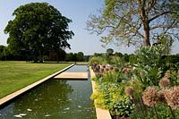 Long, modern water feature by lawn and flowering perennial border.