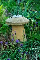 Sundial surrounded by purple flowering perennials, ferns and grasses. 