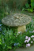 Stone mushroom sculpture surrounded by flowering herbaceous perennials.