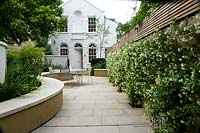 Modern, urban garden and house with pale paving and curved benching. 