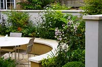Dining area and curved border in paved city garden. 