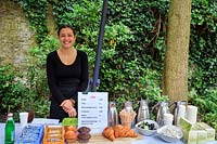 Young woman selling much-needed refreshment to the garden visitors, including coffee and croissants and muffins. The Garden of Foam Photography Museum, Amsterdam, The Netherlands. 