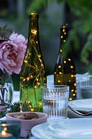 Fairylights in bottles create centrepieces on dining table in garden.
